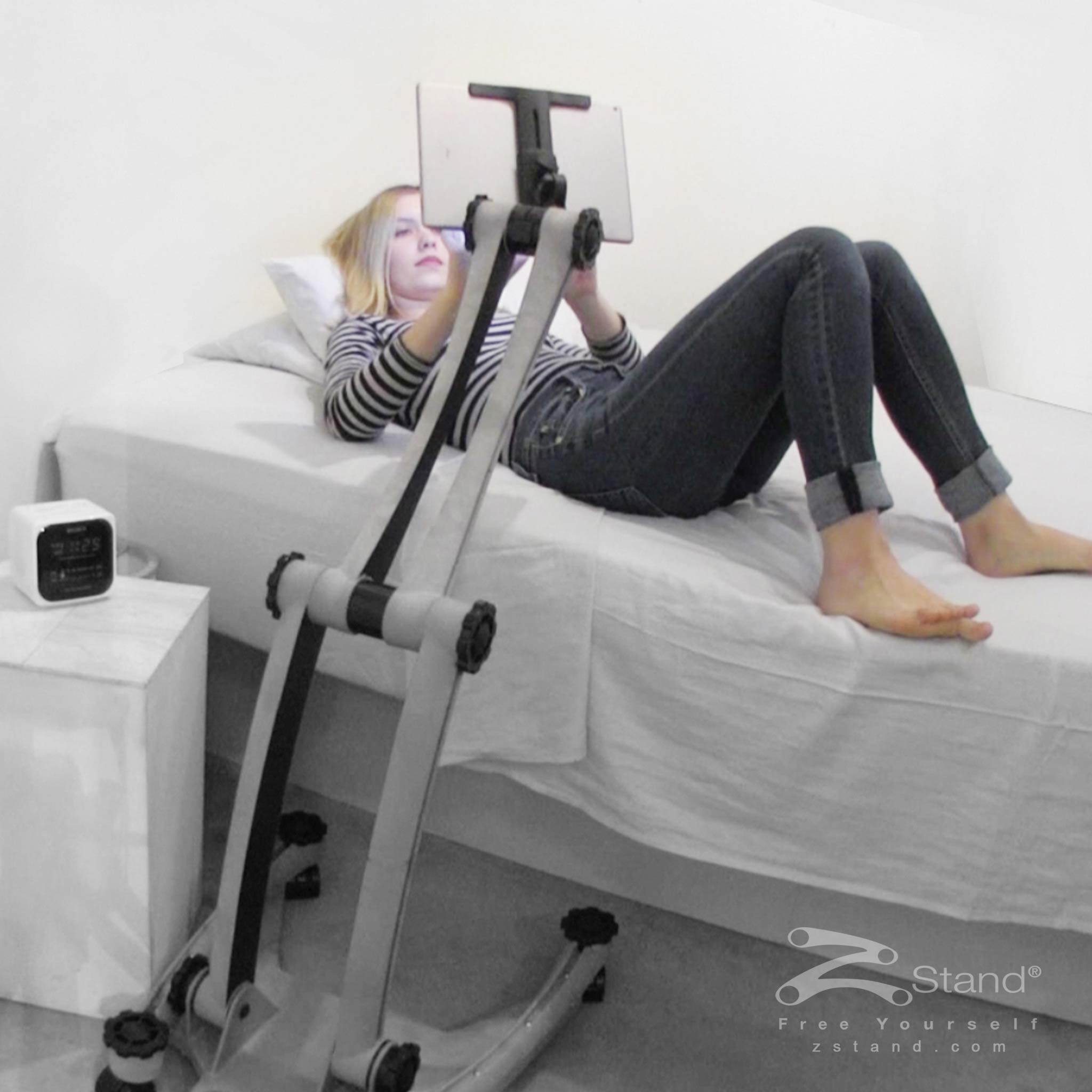 Image of a woman lying down in bed enjoying her tablet device hands free thanks to the ZStand Sportster.